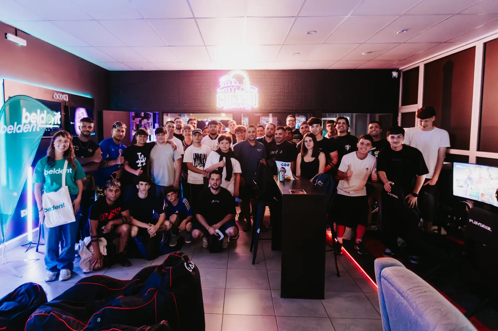La comunidad de Coliseo posando en el salón, con el cartel de neón encendido al fondo